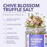 SydSalt Chive Blossom Truffle Salt in a clear glass jar with a purple label, shown next to a pile of chopped white truffles, chive blossoms, chives, lemon peel, pepper flakes, and flake salt on a light lavender background with ingredient callouts.